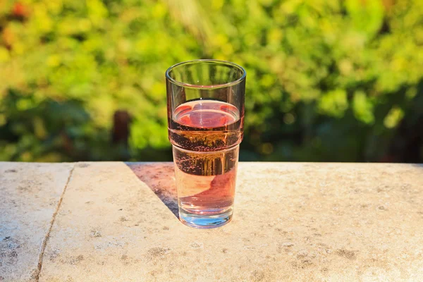 Glass of fresh pink soda on balcony with blurred green garden ba — Stock Photo, Image