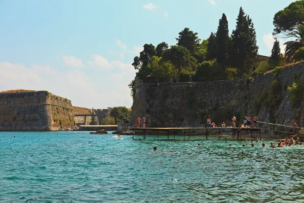 People jumping from pier in the water at the port near old fortr — Stock Photo, Image