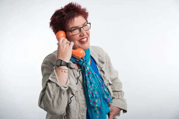 Frau mittleren Alters telefoniert mit einem orangefarbenen Telefon. roter Schuh — Stockfoto