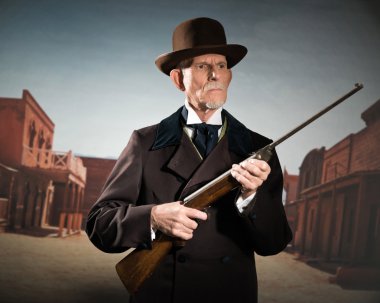 Senior western man wearing a brown hat and coat holding rifle. S clipart