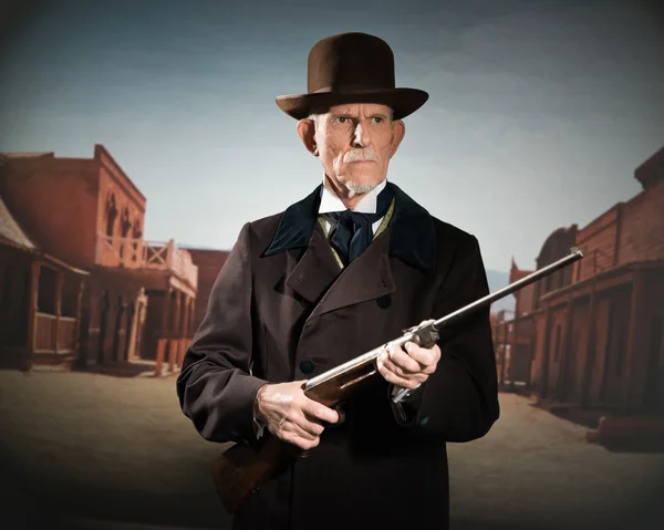 Ein älterer Mann mit braunem Hut und Mantel, der ein Gewehr in der Hand hält. s — Stockfoto