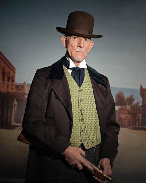 Старший вестерн в коричневой шляпе и пальто с винтовкой. S
