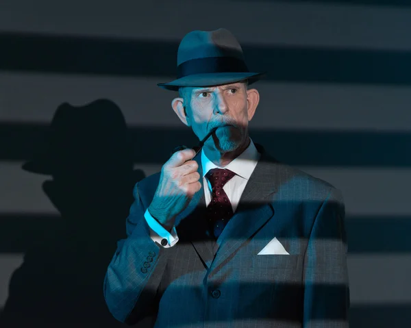 Retro detective man smoking pipe at night in office. Lit by ligh — Stock Photo, Image