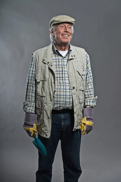 Jardinero hombre mayor sonriendo con sombrero sosteniendo cucharada. Captura de estudio —  Fotos de Stock