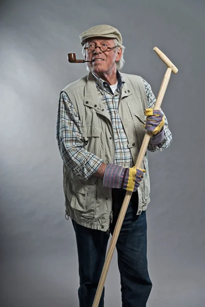 Gardener senior man with hat holding hoe. Wearing glasses and sm — Stock Photo, Image