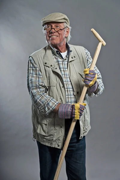 Smiling senior gardener man with hat holding hoe. Wearing glasse — Stock Photo, Image