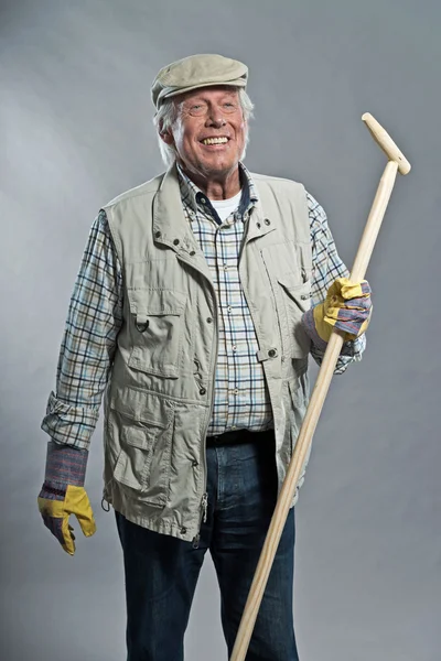 Leende senior trädgårdsmästare man med hatt hålla hoe. Studio skott ag — Stockfoto