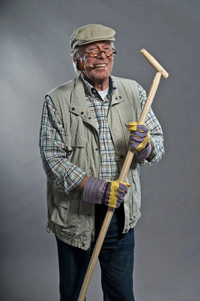 Gardener senior man with hat holding hoe. Wearing glasses and sm — Stock Photo, Image