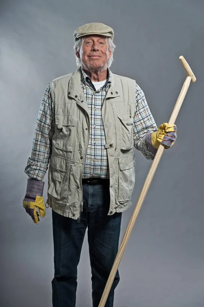 Un giardiniere anziano sorridente con la zappa sul cappello. Studio girato ag — Foto Stock