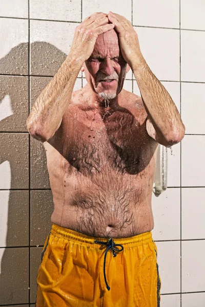 Senior man taking a shower in bathroom. Wearing yellow swimming — Stock Photo, Image