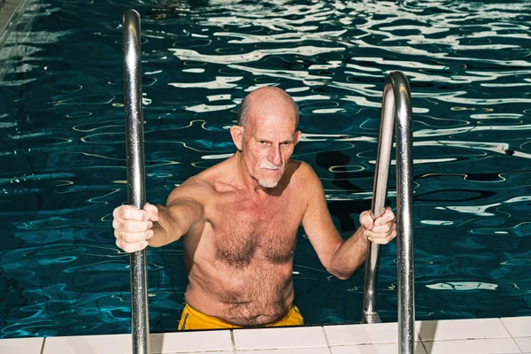 Senior man walking out of swimming pool. Wearing yellow swimming — Stock Photo, Image