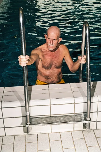 Senior man walking out of swimming pool. Wearing yellow swimming — Stock Photo, Image