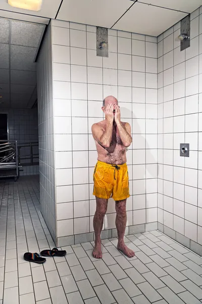 Senior man taking a shower in bathroom. Wearing yellow swimming — Stock Photo, Image