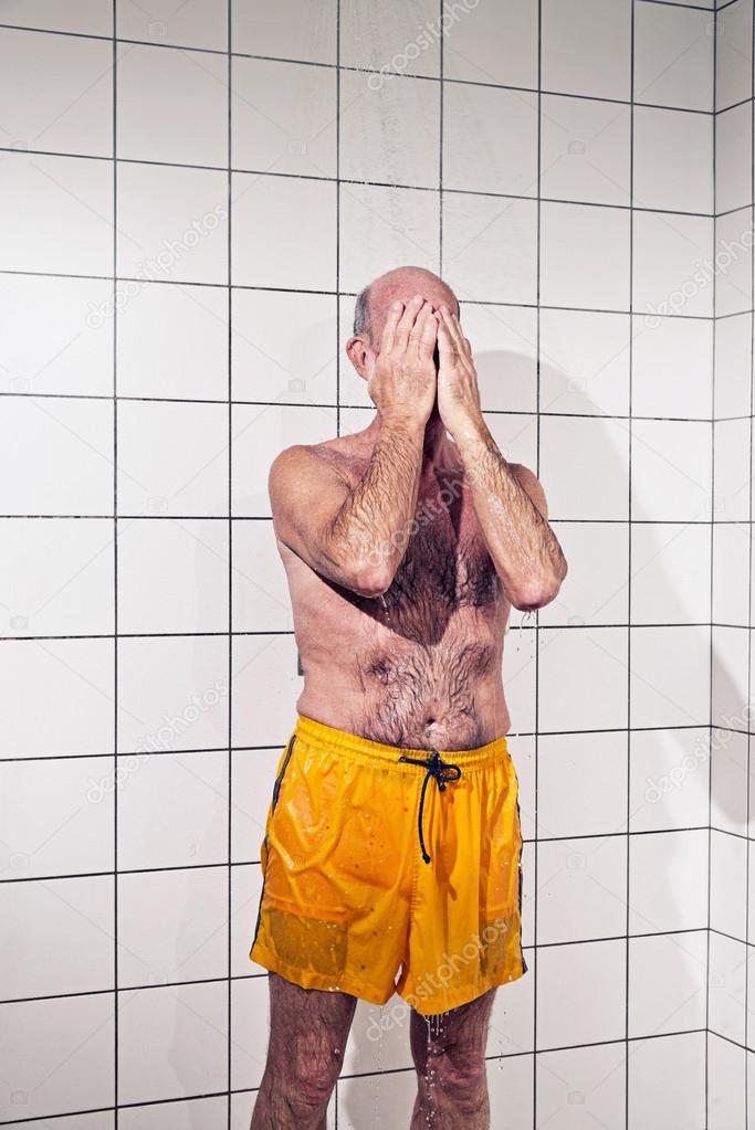 Senior man taking a shower in bathroom. Wearing yellow swimming
