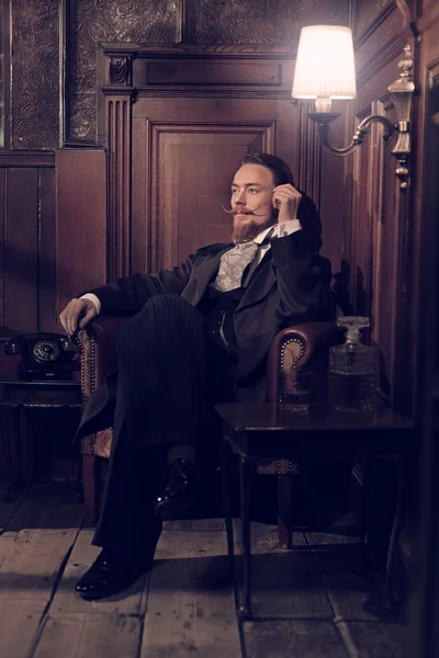 Vintage 1900 homem de moda com barba. Sentado em velho readi de madeira — Fotografia de Stock