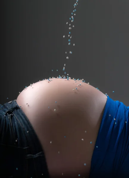 Pregnancy belly sprinkled with white and blue birth candies. Clo