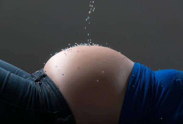 Pregnancy belly sprinkled with white and blue birth candies. Clo — Stock Photo, Image