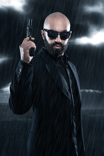 Dangerous bald gangster man with beard holding gun. Wearing blac — Stock Photo, Image