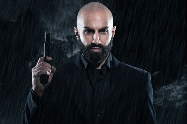Peligroso hombre gángster calvo con barba sosteniendo arma. Usando blac — Foto de Stock
