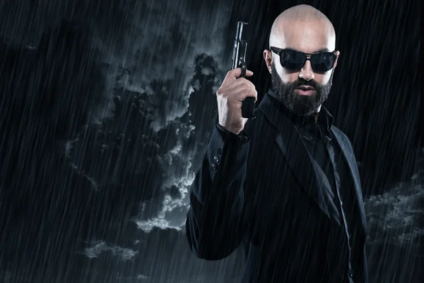 Dangerous bald gangster man with beard holding gun. Wearing blac — Stock Photo, Image