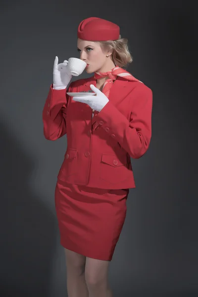 Ретро блондинка стюардеса в червоному костюмі з шапочкою. Випив кусень — стокове фото