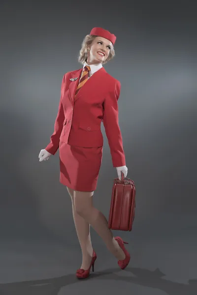 Χαμογελώντας ρετρό ξανθιά αεροσυνοδός φοράει κόκκινο κοστούμι με ριγέ τι — Φωτογραφία Αρχείου