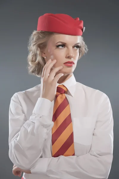 Seriöse retro blonde Stewardess mit roter Mütze und gestreifter Krawatte — Stockfoto