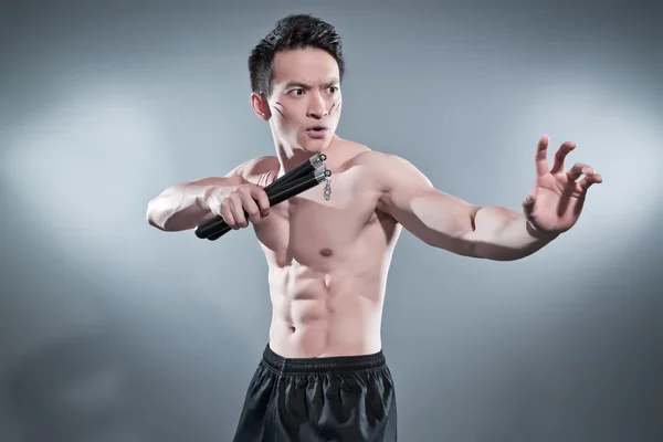 Svalnatý asijské kung-fu muž v akci představovat s nunchucks. krev s — Stock fotografie