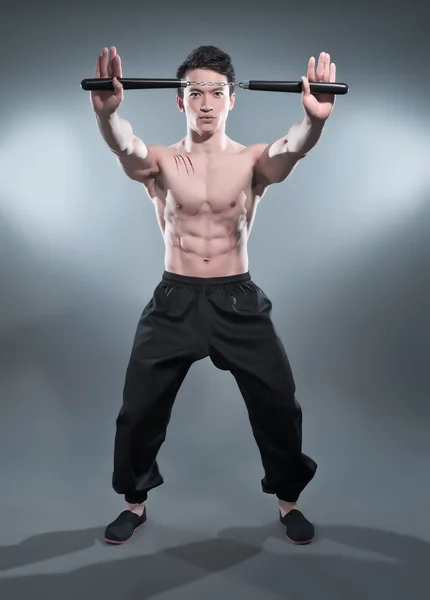 Muscled asian kung fu man in action pose with nunchucks. Blood s — Stock Photo, Image