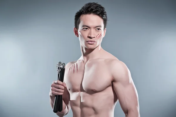 Musculoso asiático kung fu hombre con nunchucks. Arañazos de sangre en su —  Fotos de Stock