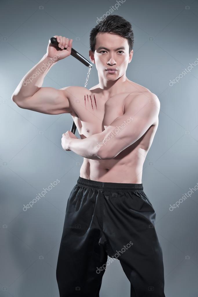 Muscled asian kung fu man in action pose with nunchucks. Blood s Stock