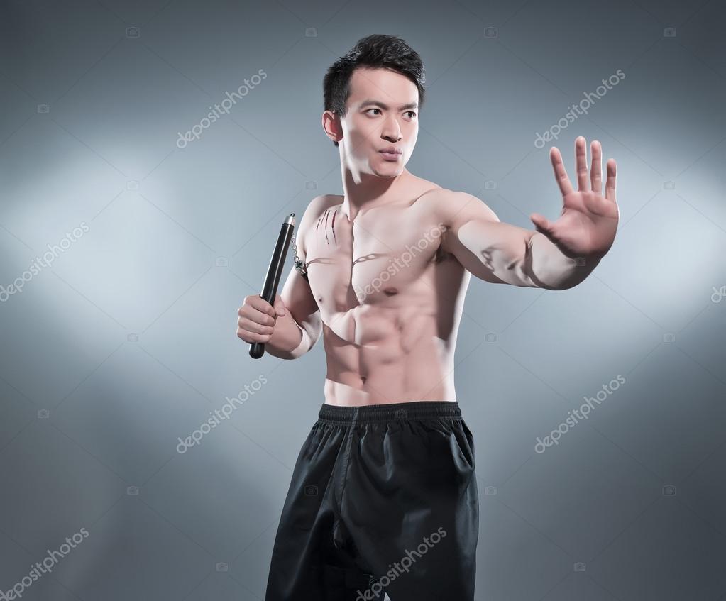 Muscled asian kung fu man in action pose with nunchucks. Blood s Stock