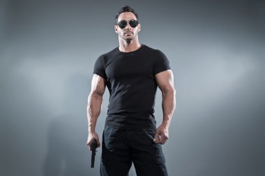 Action hero muscled man holding a gun. Wearing black t-shirt wit