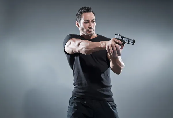 Action hero muscled man shooting with gun. Wearing black t-shirt — Stock Photo, Image