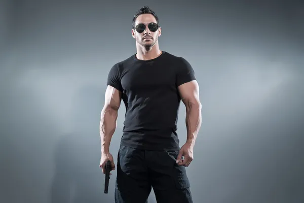 Action hero muscled man holding a gun. Wearing black t-shirt wit — Stock Photo, Image