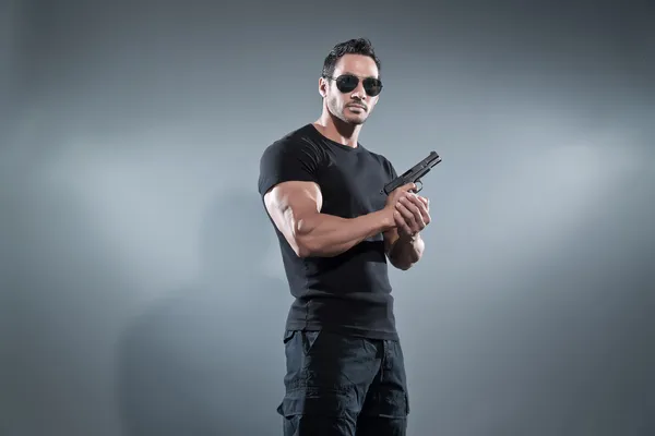 Homem musculado herói de ação segurando uma arma. Vestindo camiseta preta sagacidade — Fotografia de Stock