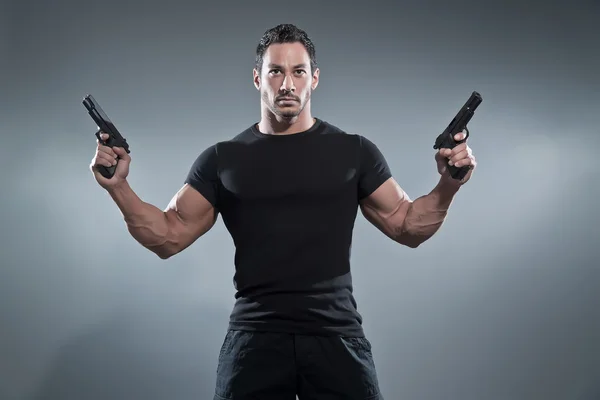 Action hero muscled man holding two guns. Wearing black t-shirt — Stock Photo, Image