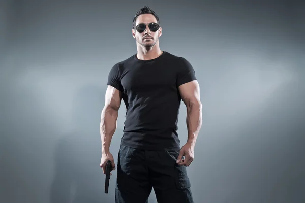 Action hero muscled man holding a gun. Wearing black t-shirt wit Royalty Free Stock Images