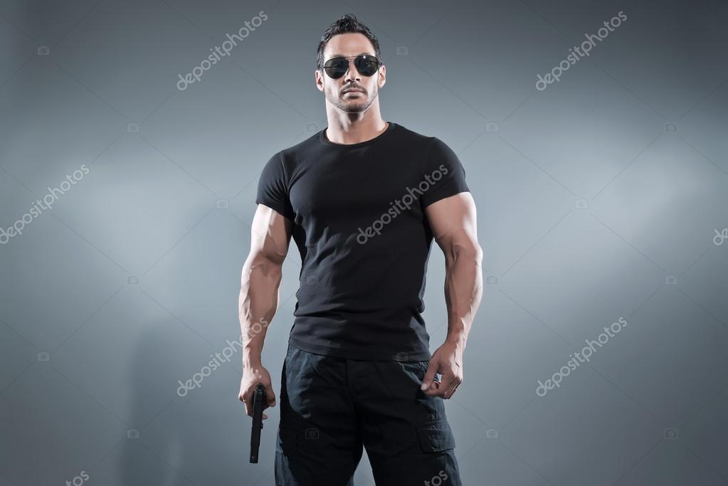 Infecteren maniac Kruik Action hero muscled man holding a gun. Wearing black t-shirt wit Stock  Photo by ©ysbrand 47501513