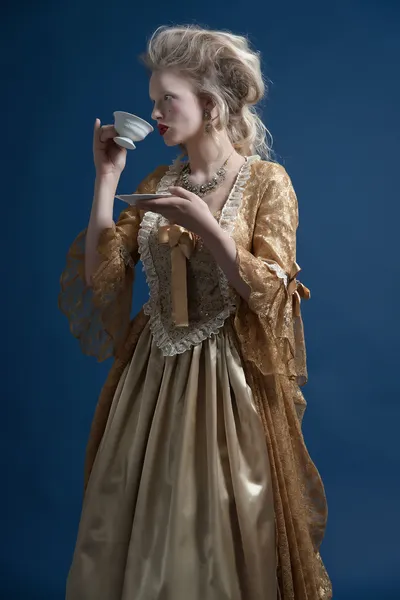 Retro baroque fashion woman wearing gold dress. Holding a cup of — Stock Photo, Image