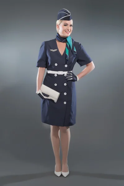 Smiling retro blonde stewardess wearing blue suit. Holding white — Stock Photo, Image