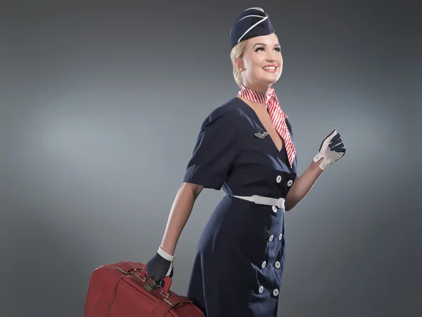 Smiling retro blonde stewardess wearing blue suit. Holding red l — Stock Photo, Image