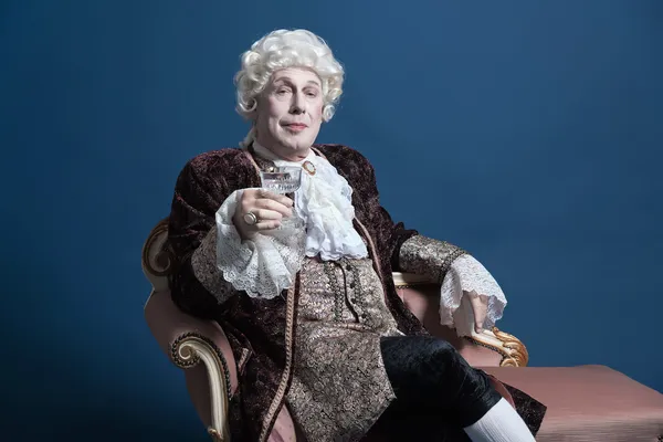 Retro baroque man with white wig holding a wine glass sitting on — Stock Photo, Image