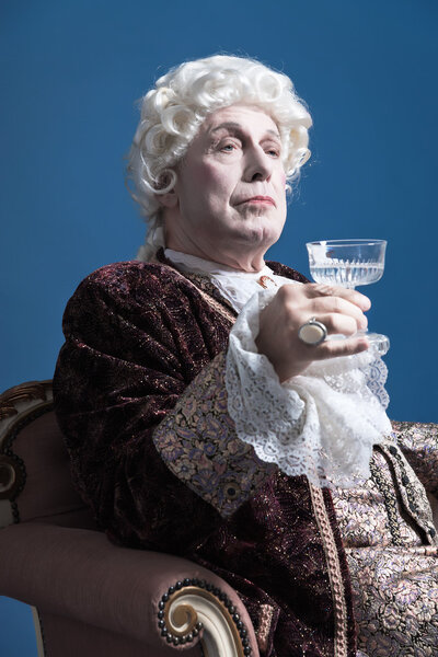 Retro baroque man with white wig holding a wine glass sitting on