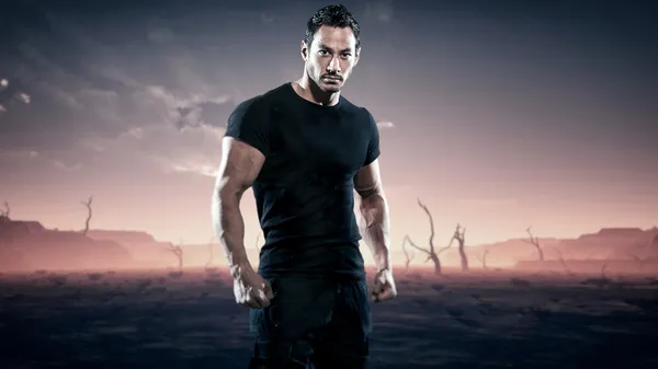 Strong muscled hero fitness man standing in desolate landscape w — Stock Photo, Image