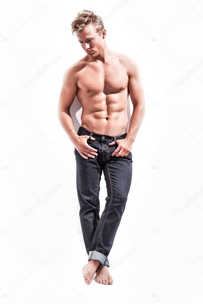 Male fitness model wearing blue jeans. Blonde hair. Against whit