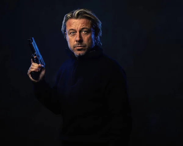 自信のある男の影の夜の肖像画彼の手に銃を持つブロンドの髪 黒いウールのセーター — ストック写真