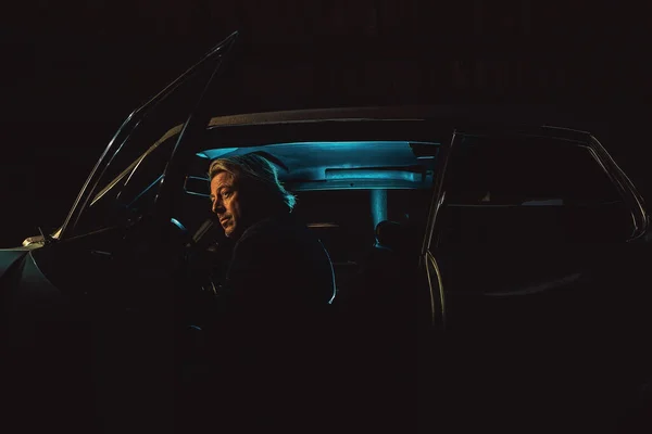 一个金发碧眼的男人晚上坐在一辆美国经典的肌肉车里面 — 图库照片