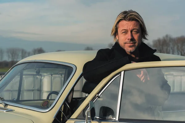 男で黒コートにブロンド髪と頑丈スタンドによって古典的な車で日当たりの良い田舎 — ストック写真