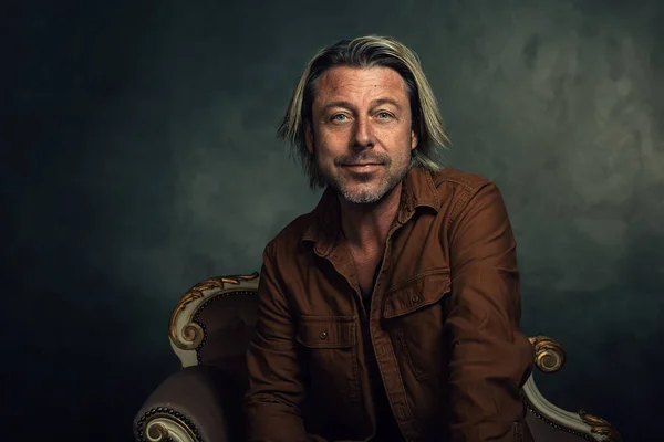 Smiling Man Blond Hair Brown Shirt Sits Sofa Front Dark — Fotografia de Stock